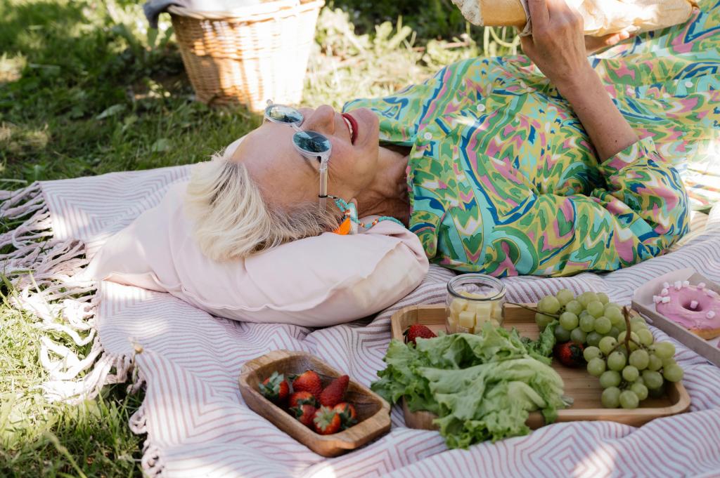 Ältere Dame liegt auf einer Picknickdecke mit Snacks wie Erdbeeren, Salat, Käse und Weintrauben.